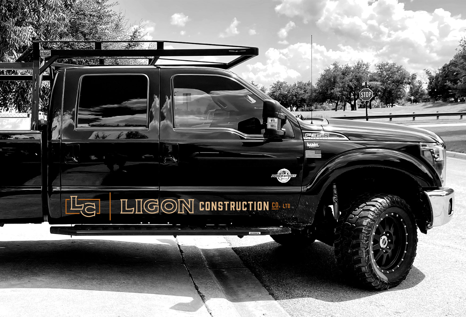 ligon construction truck decal design by beau morrow for left hand design in austin texas. A black Ford F-250 Super Duty truck with large off-road tires is parked on a street, featuring “Ligon Construction Co. Ltd.” branding in bold orange lettering on the driver-side door. The truck has a rugged roof rack and decals including a U.S. flag and “Power Stroke” emblem, indicating heavy-duty capability.